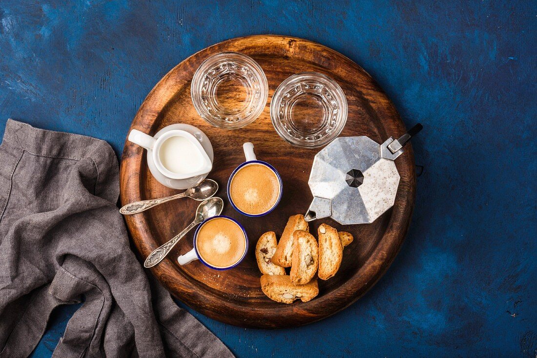 Coffee espresso in cups with italian cantucci, cookies and milk in jug on wooden serving round board