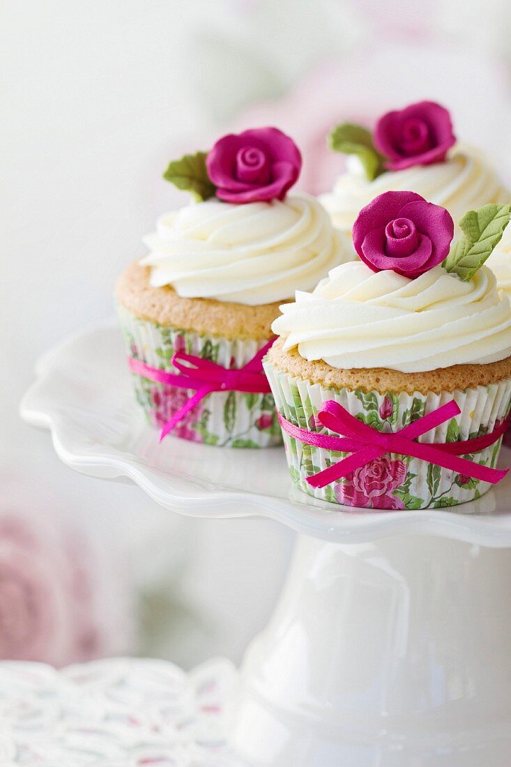 Mit rosa Zuckerrose verzierte Cupcakes auf einem Kuchenständer
