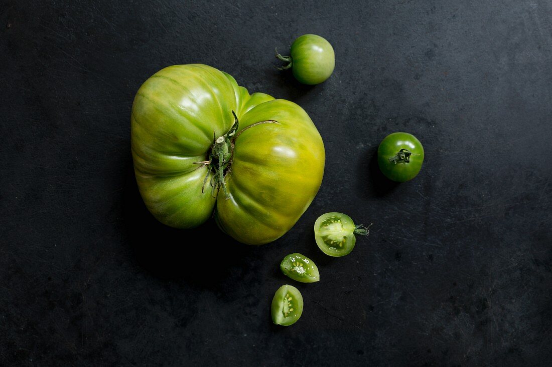 Two varieties of green tomatoes on a dark metal surface (varieties: Green Doctor and Absinthe)