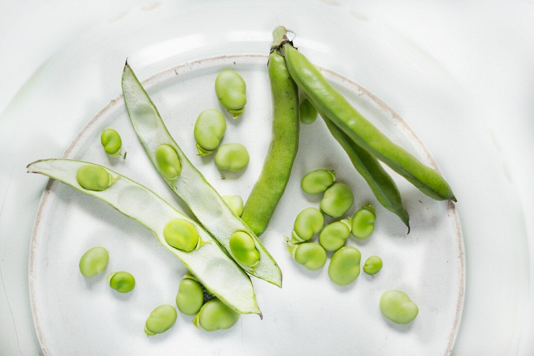 Broad bean pods, some opened and with the beans removed, in a ceramic dish
