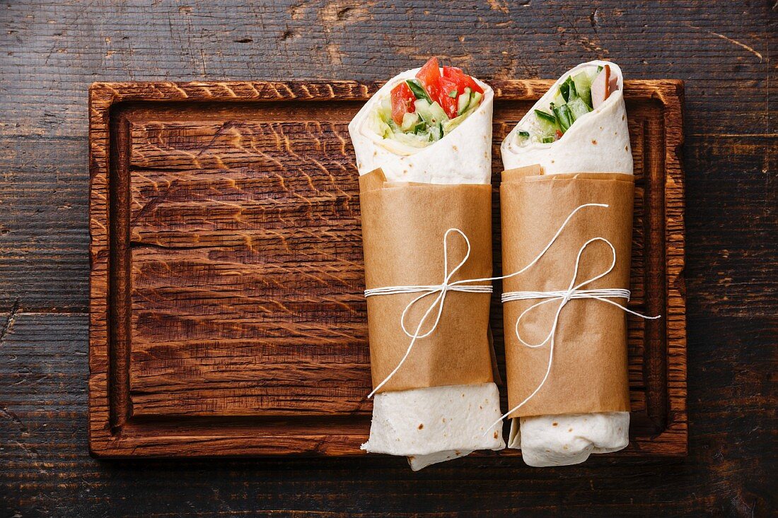 Tortilla wraps sandwiches with fresh vegetables on wooden cutting board