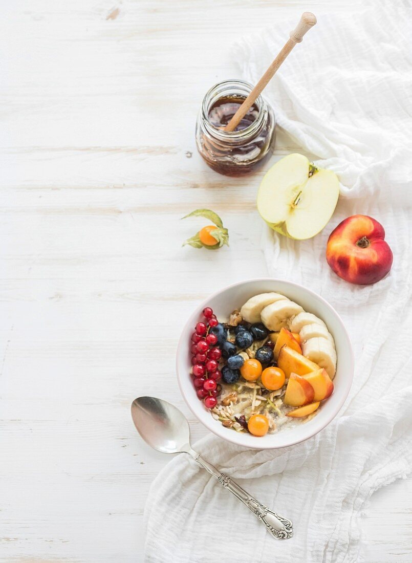 Bircher muesli with fresh friut, berries and honey over white painted wooden background