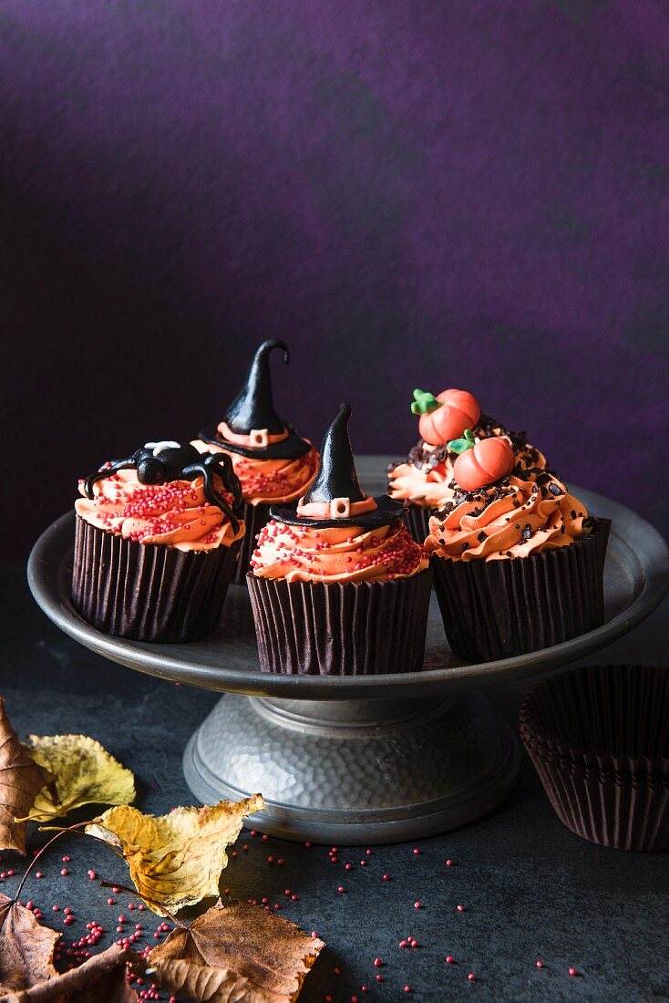 Halloween-Cupcakes mit orangefarbener Buttercreme und verschiedenen Fondant-Dekos auf einem Kuchenständer