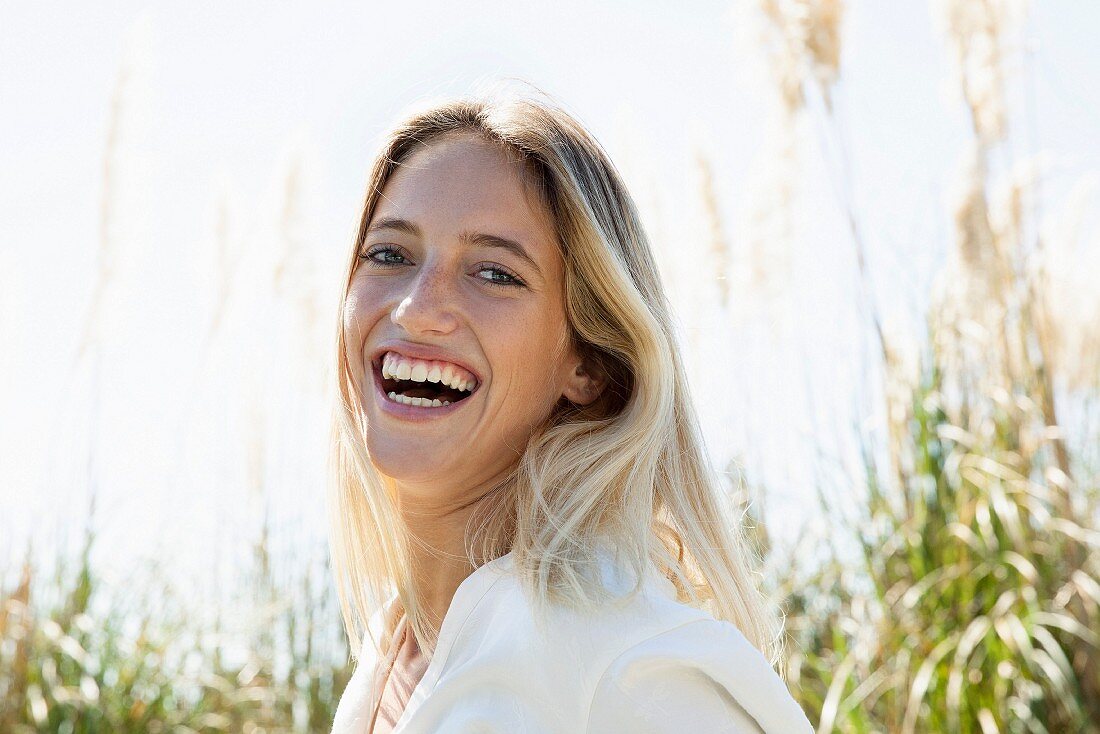 A blonde woman laughing outdoors