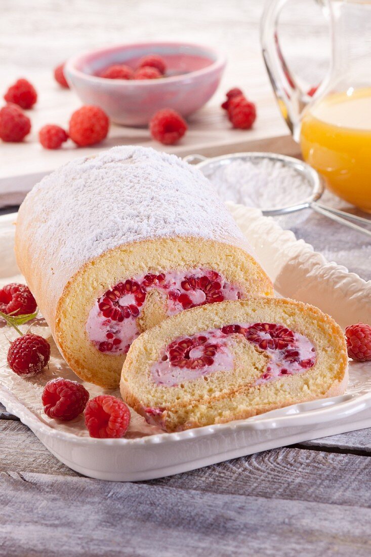 A Swiss roll with raspberries and icing sugar
