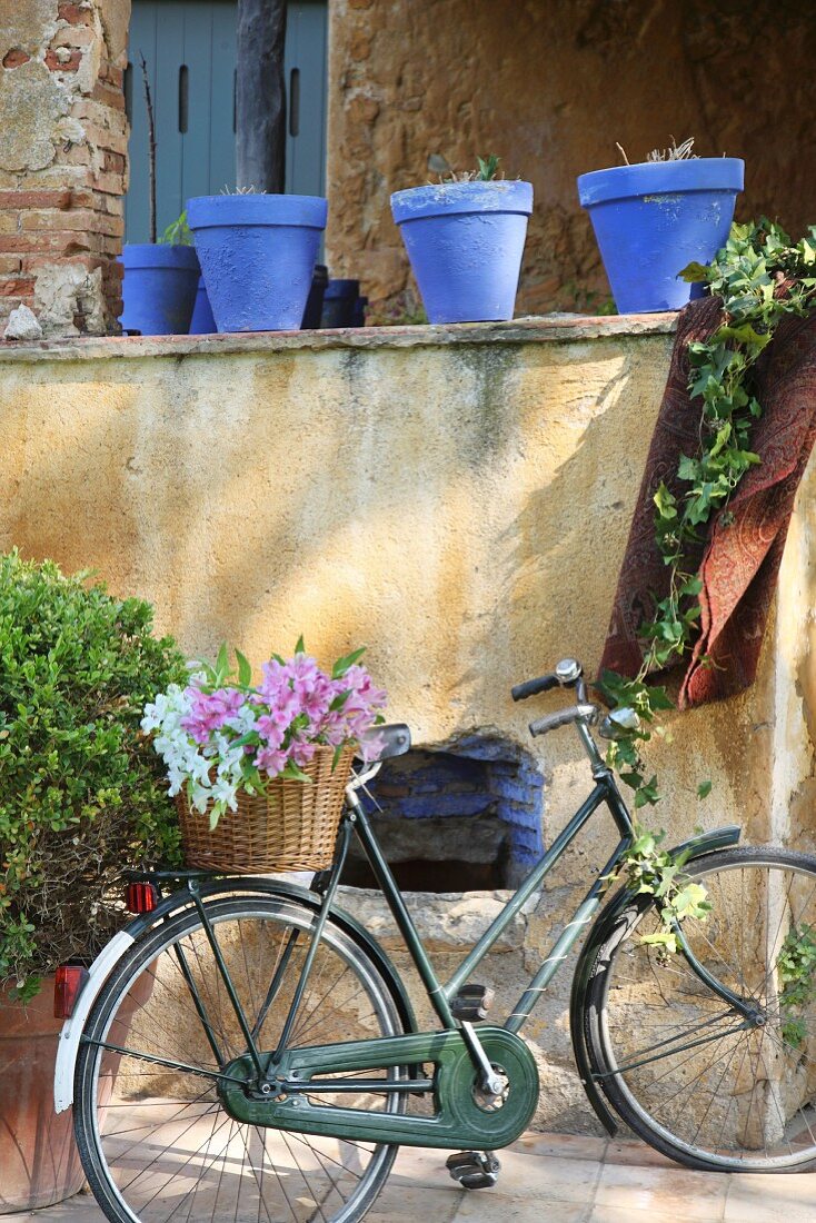 Damenrad mit Blumenkorb vor Mauer mit blauen Blumentöpfen