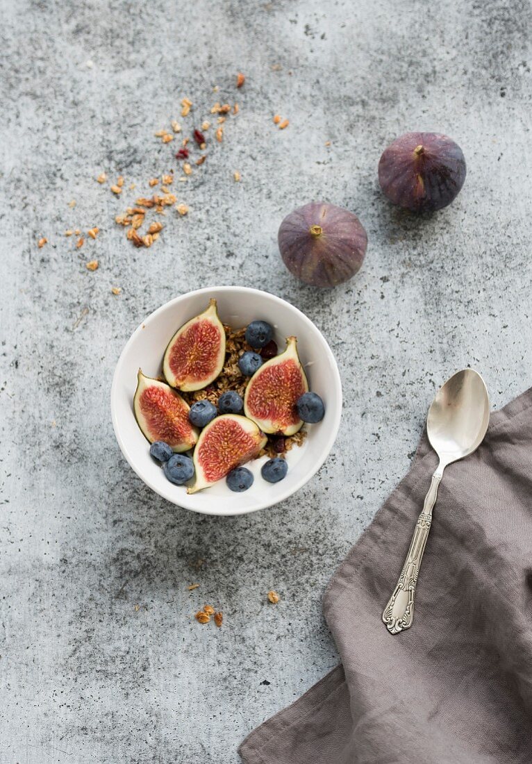 Oat granola crumble with fresh figs and blueberrie in white bowl on grunge grey backdrop