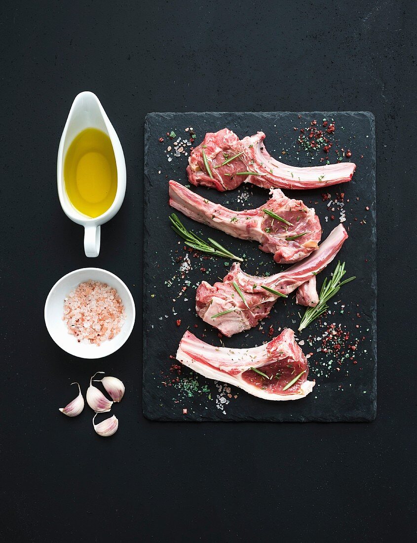 Raw uncooked lamb ribs with olive oil, spices and garlic on dark board ober black background