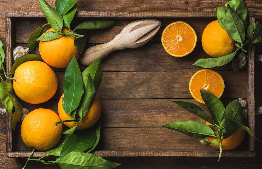 Frische Orangen mit Blättern und Zitruspresse aus Holz auf Holztablett