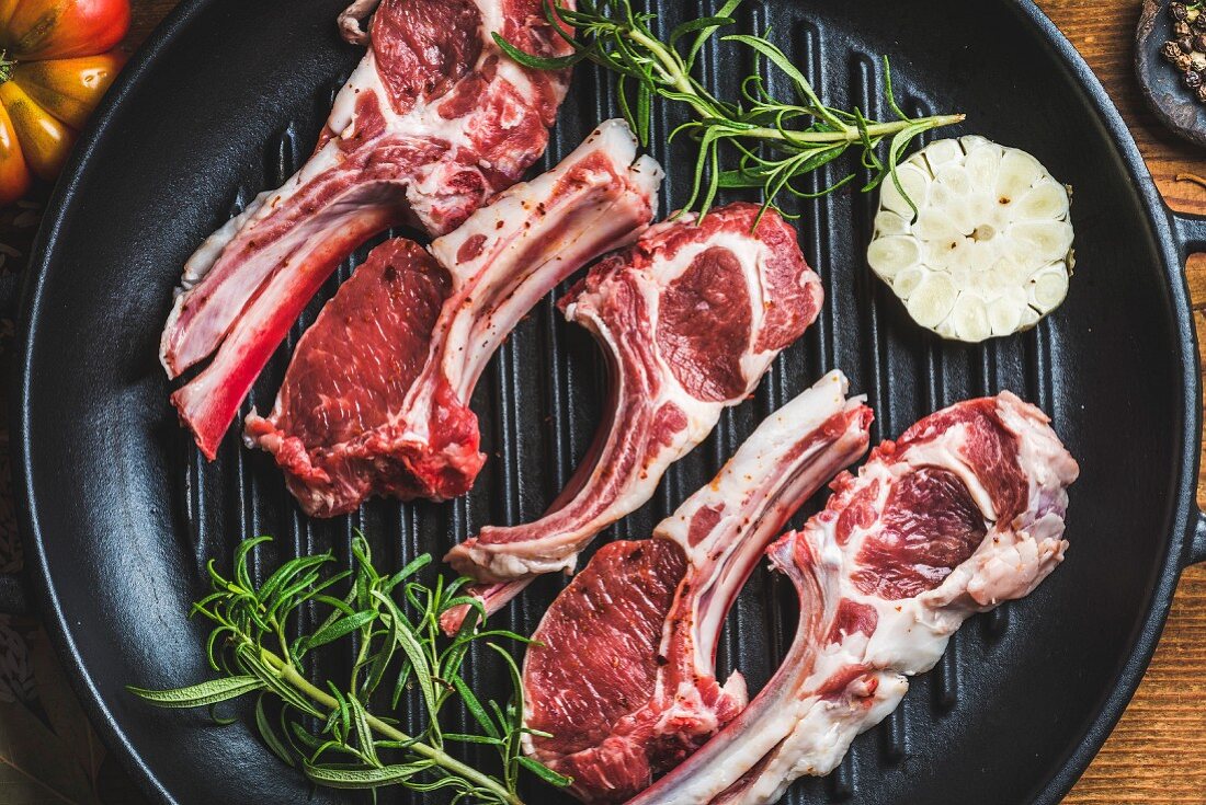 Raw uncooked lamb meat chops with rosemary and garlic in black iron grilling pan