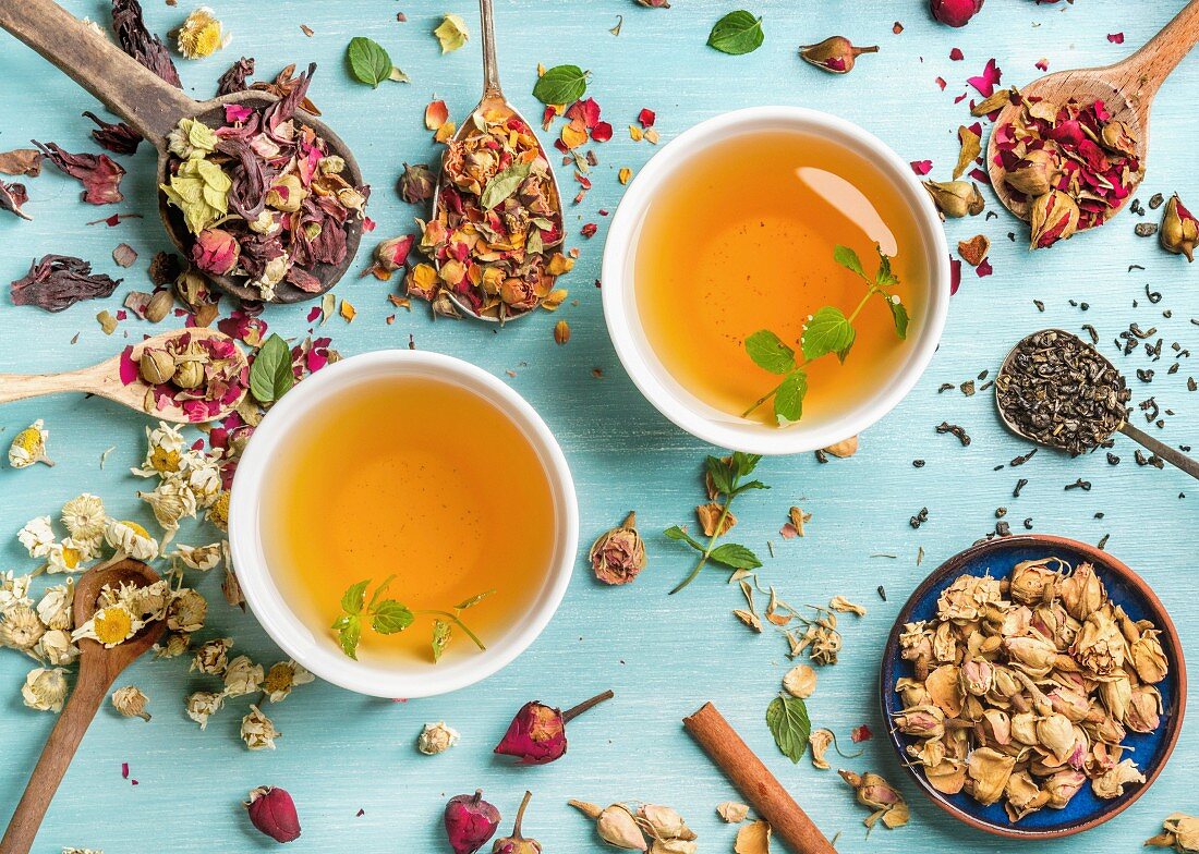 Two cups of healthy herbal tea with mint, cinnamon, dried rose and camomile flowers in spoons