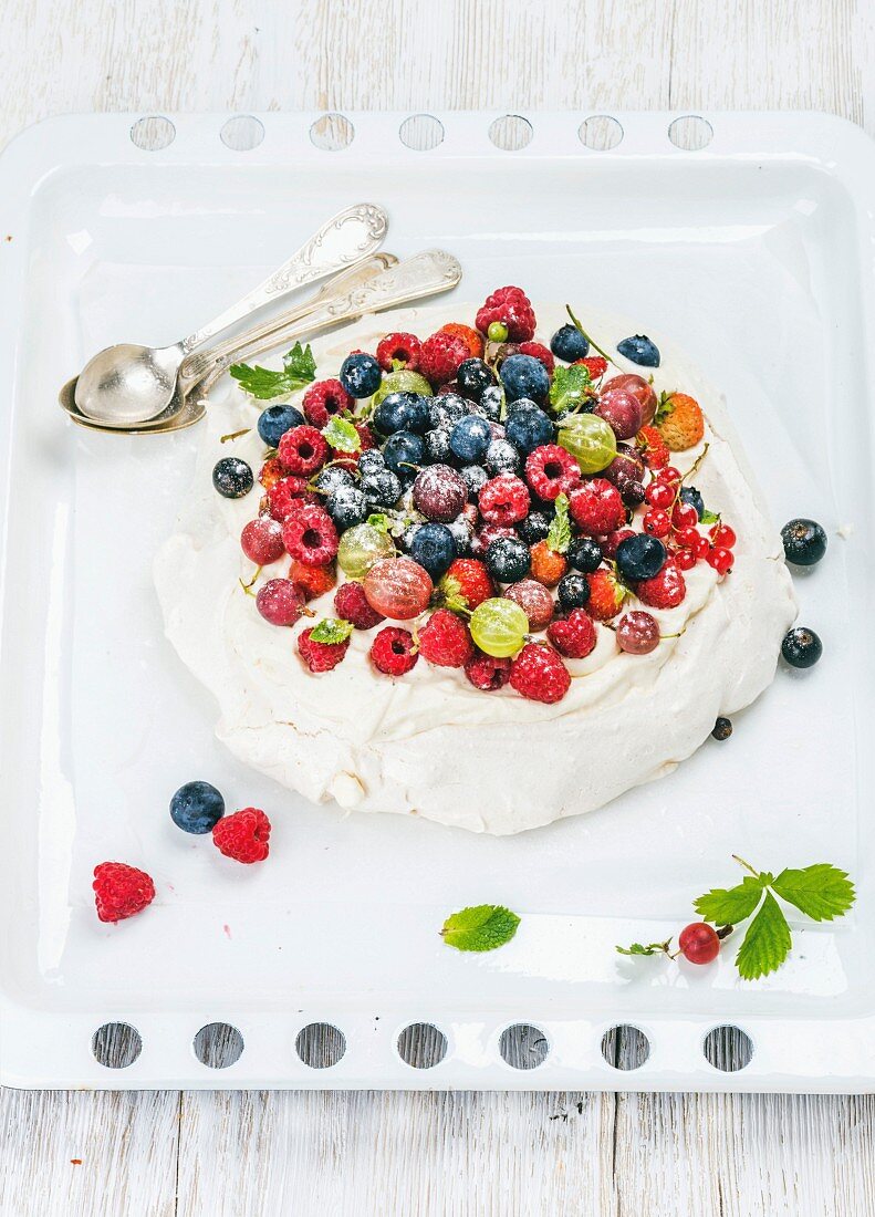 Homemade Pavlova cake with fresh garden berries served with silver spoons on white baking tray