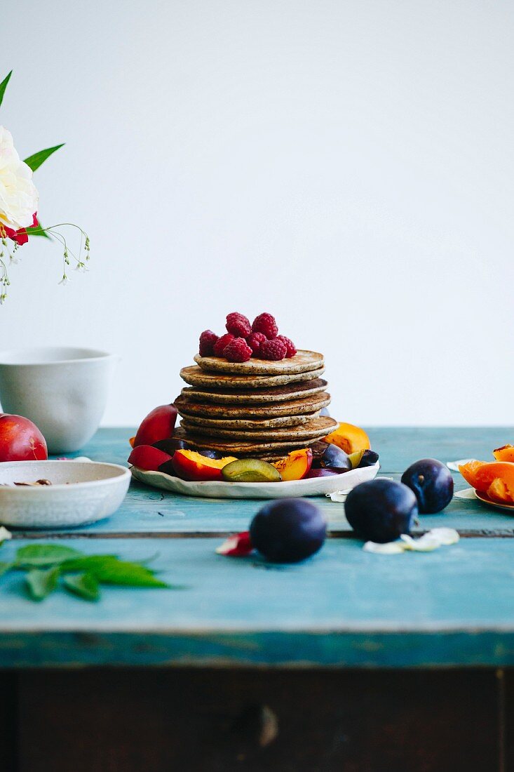 Gestapelte Pancakes mit Früchten garniert auf türkis Holztisch