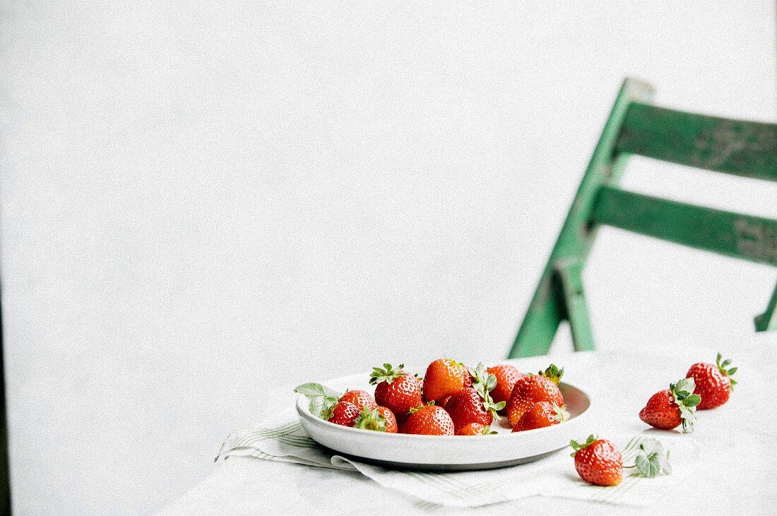 A table scene with strawberries and a green chair