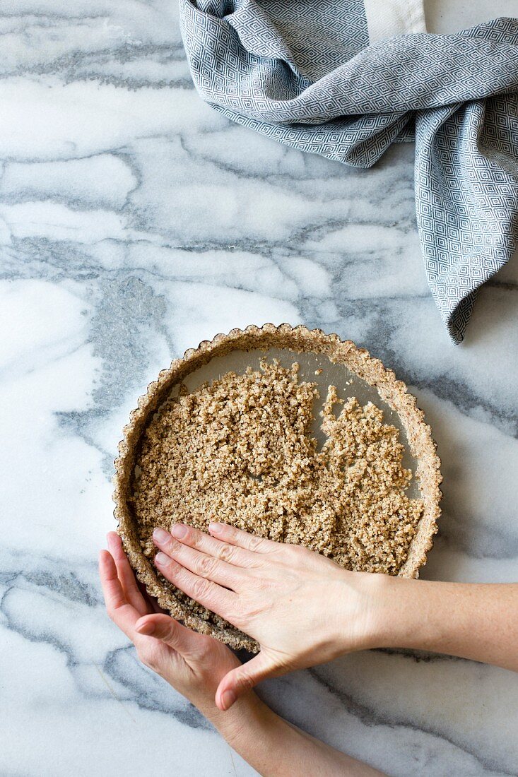 Person prepares a gluten free tart crust, made from sliced almonds, shredded coconut, salt and maple syrup