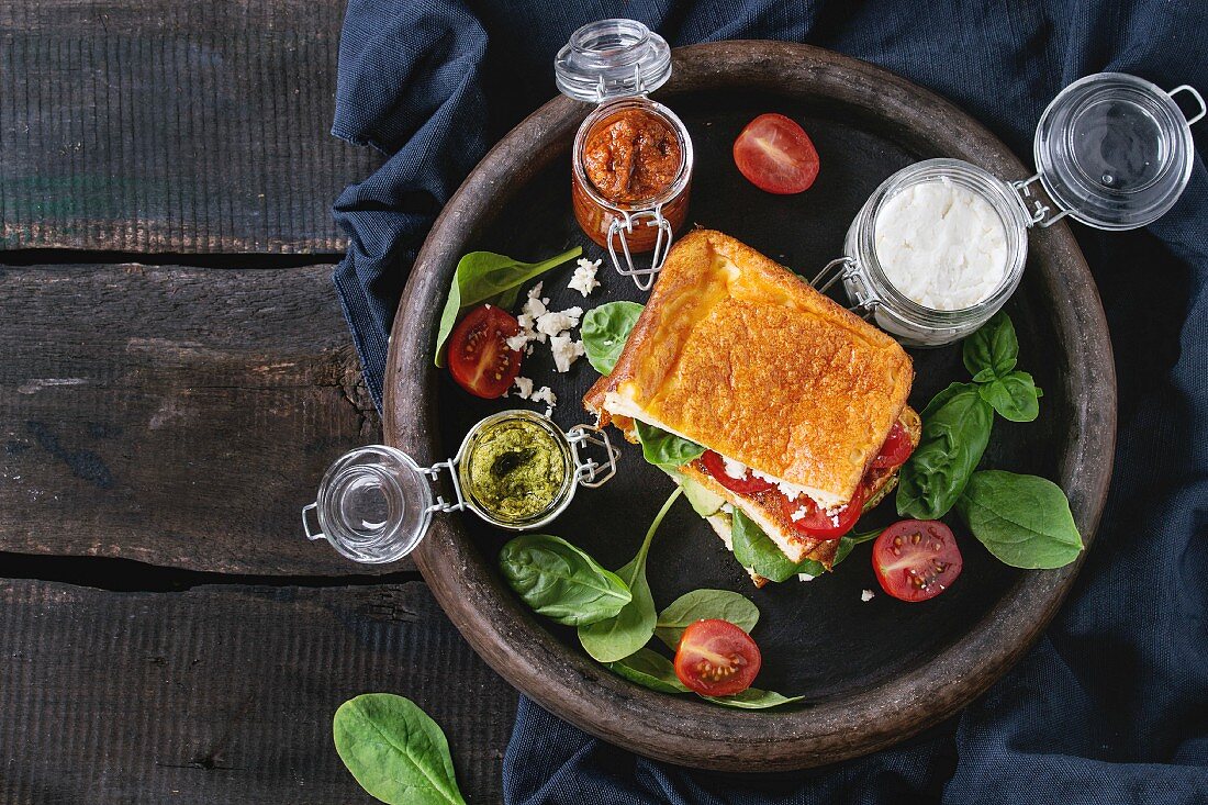 A low-carb gluten-free cloud bread sandwich with spinach, avocado, feta cheese, tomatoes and pesto