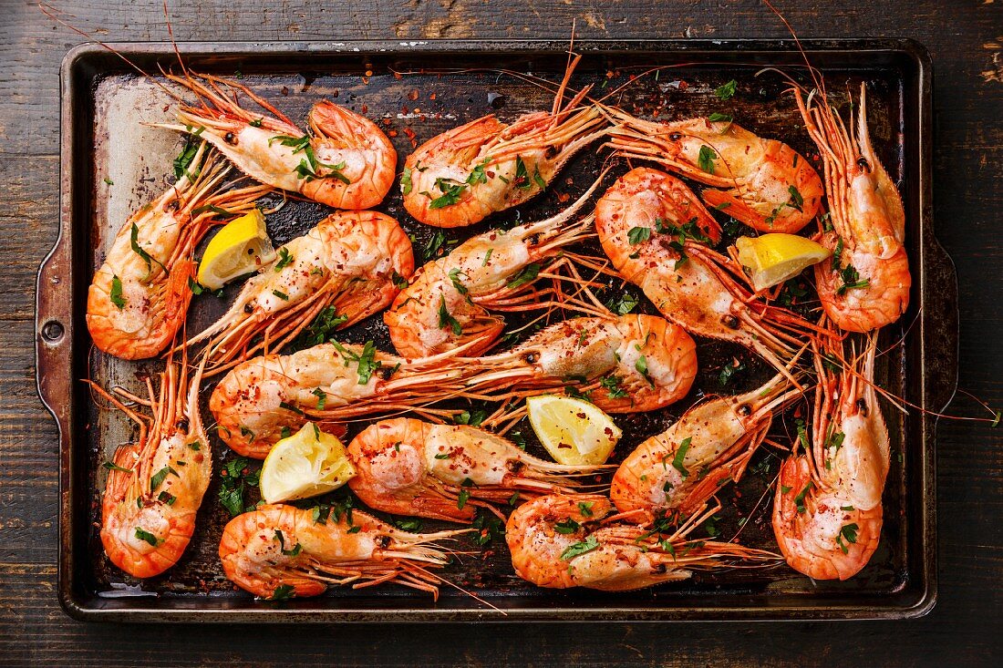 Roasted shrimp comb with greens, spices and lemon on metal baking sheet background