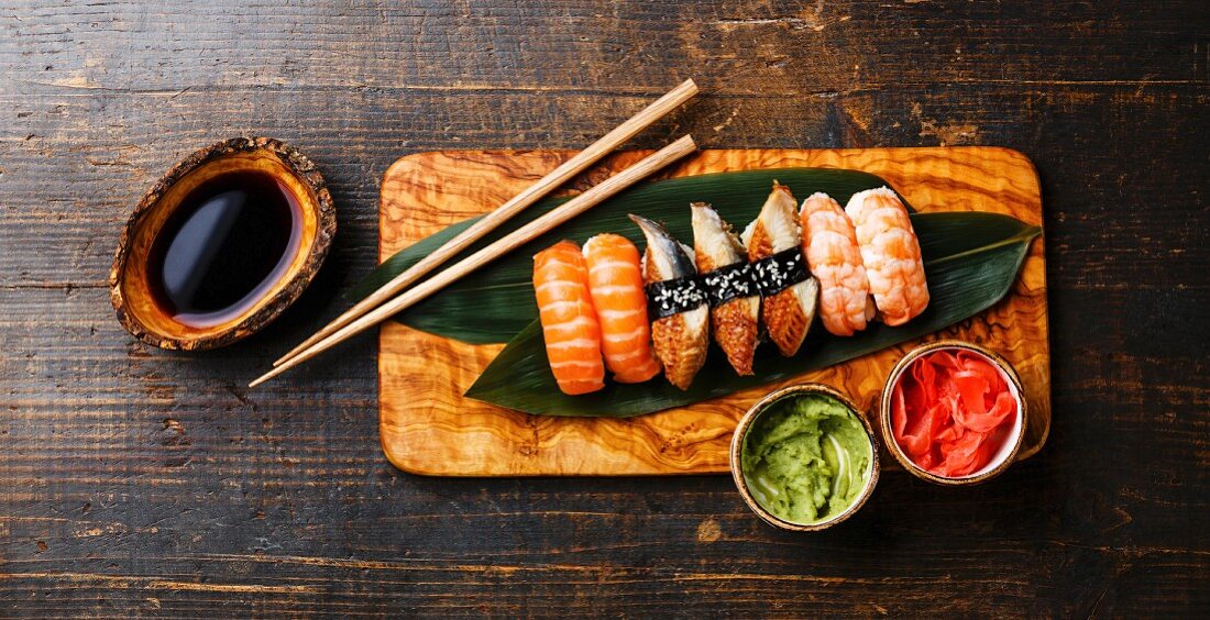 https://media02.stockfood.com/largepreviews/MzcxODkzMjY3/11996557-Nigiri-Sushi-Set-on-bamboo-green-leaf-on-olive-wood-board-with-soy-sauce-on-wooden-background.jpg