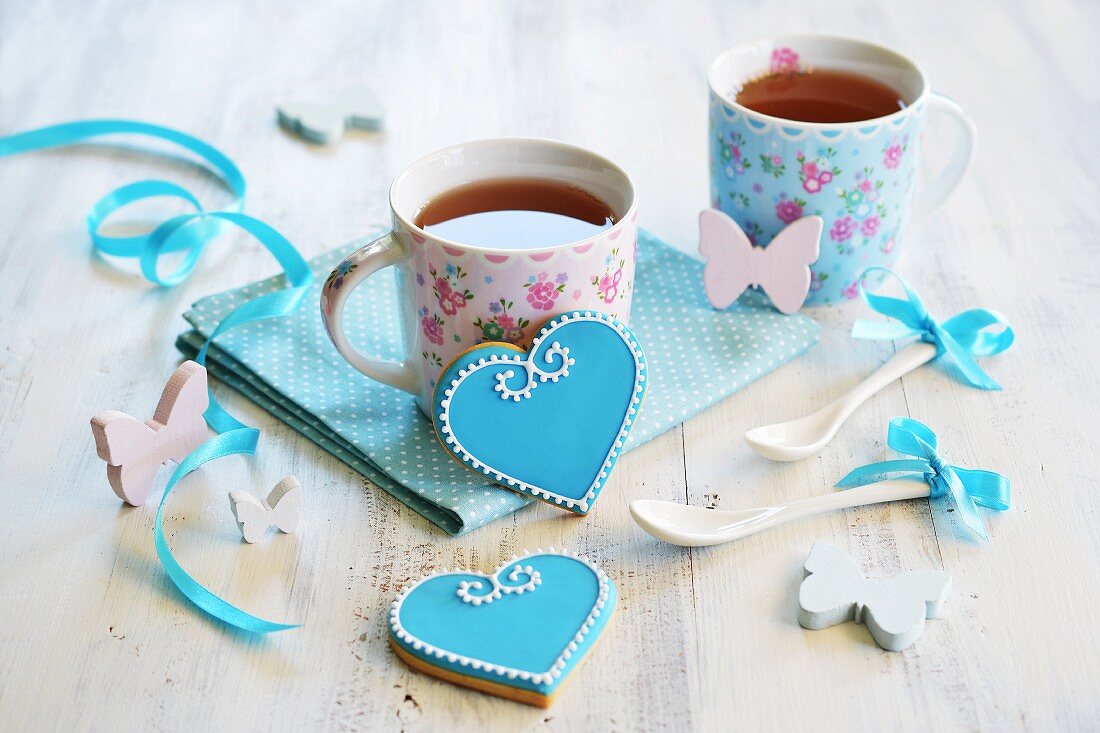 Heart-shaped biscuits decorated with blue and white icing and served with two cups of tea