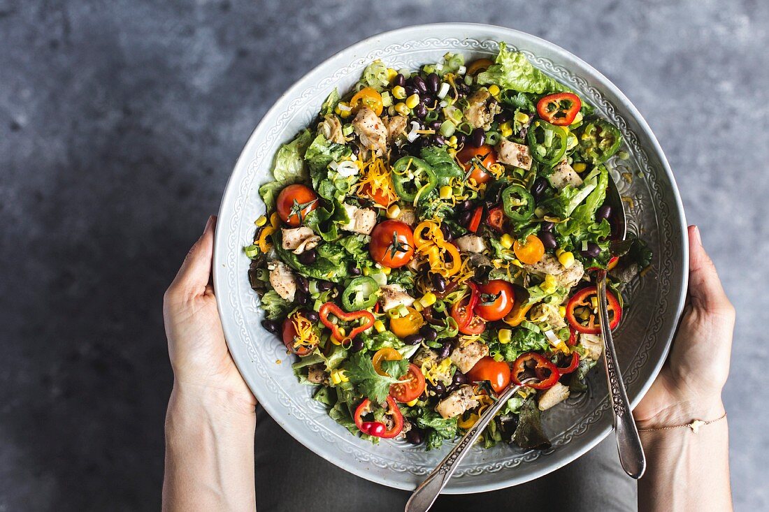 Hands holding a bowl of southwestern chicken salad with avocado dressing