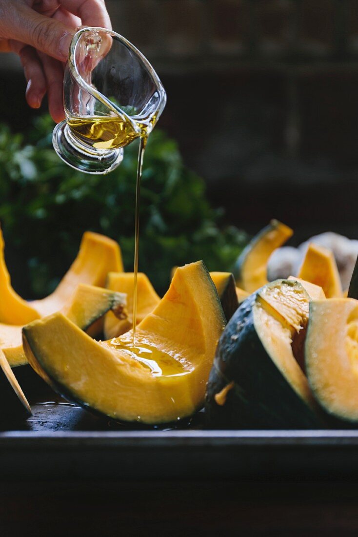 Wedges of kabocha squash being drizzled with olive oil