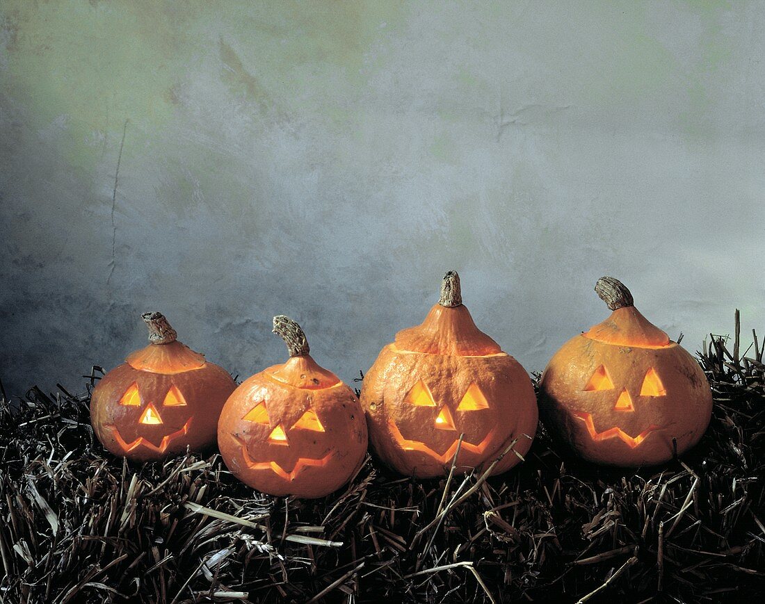 Vier leuchtende Halloweenkürbisse auf Strohballen