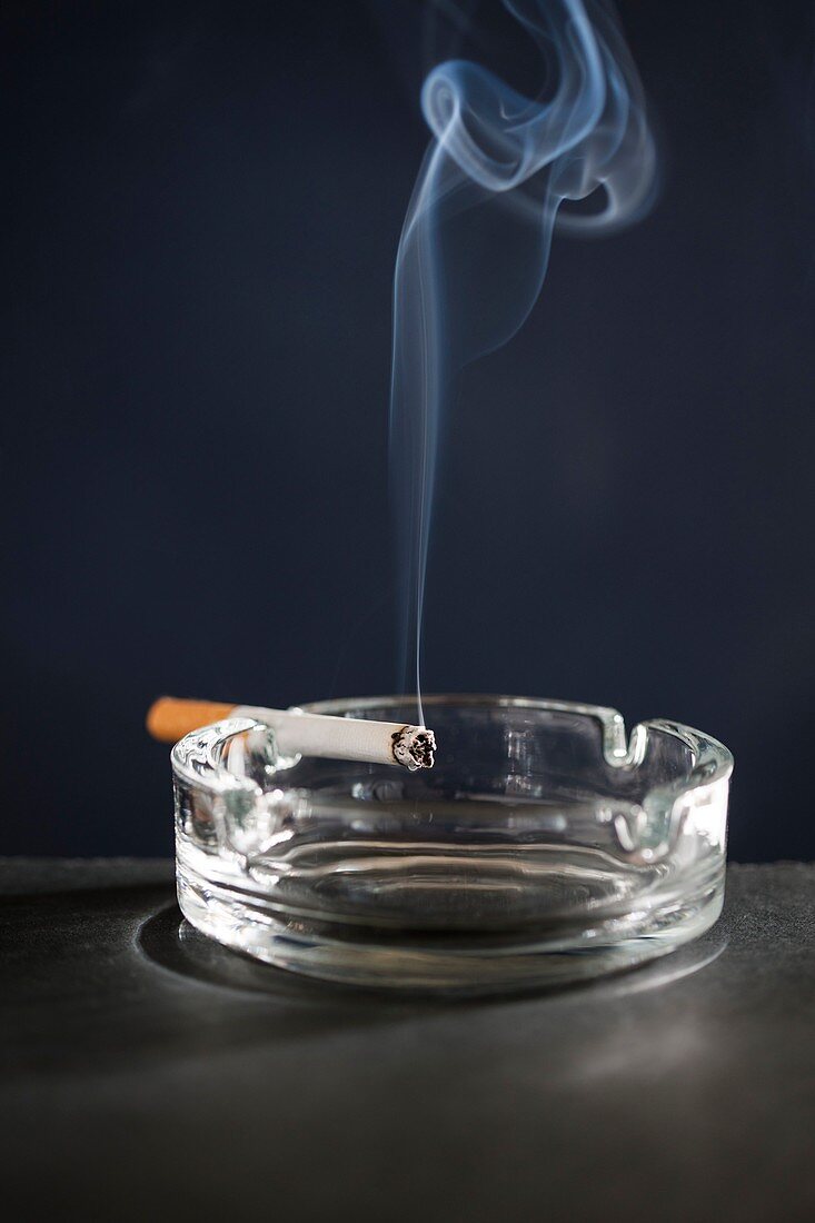 Cigarette on ash tray with smoke