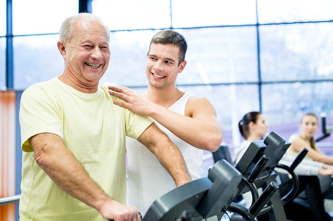Young man assisting senior man in gym