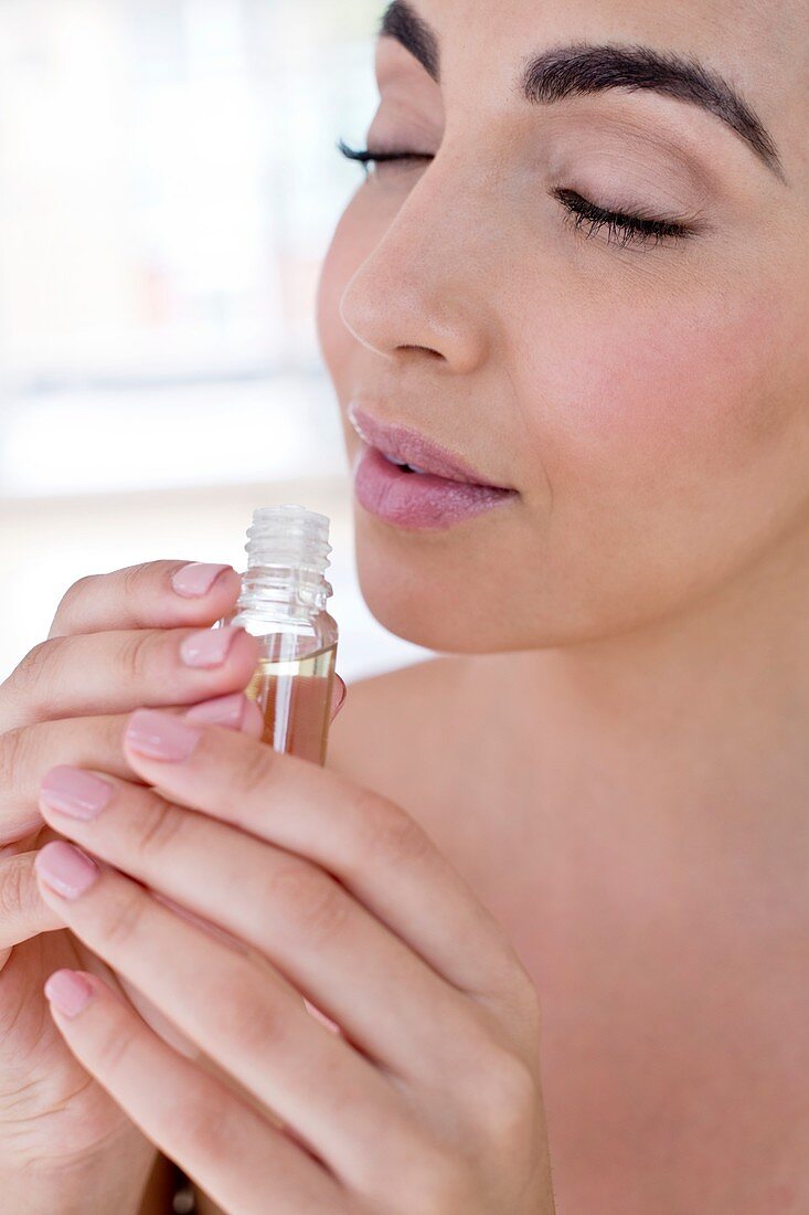 Woman smelling liquid in small glass bottle