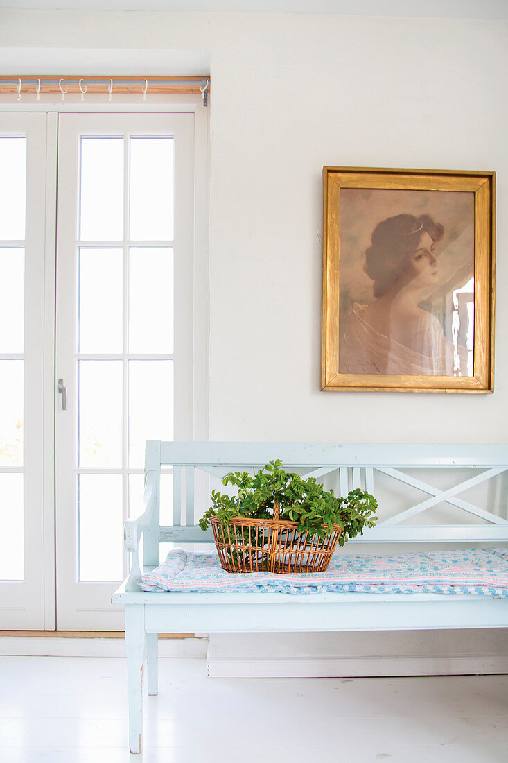 Basket of leafy branches on wooden bench below gilt-framed portrait