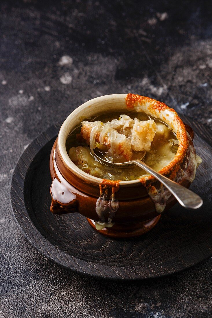 Authentic French Onion soup with dried bread and cheddar cheese in bowl on dark background