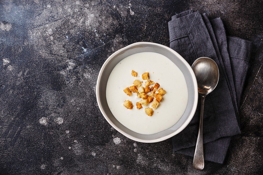 Vichyssoise cream soup in bowl with croutons on dark background