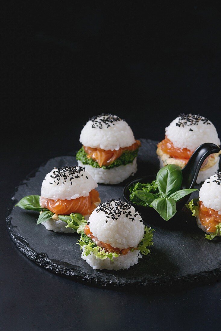 Mini rice sushi burgers with smoked salmon, green salad and sauces, black sesame served on slate stone board