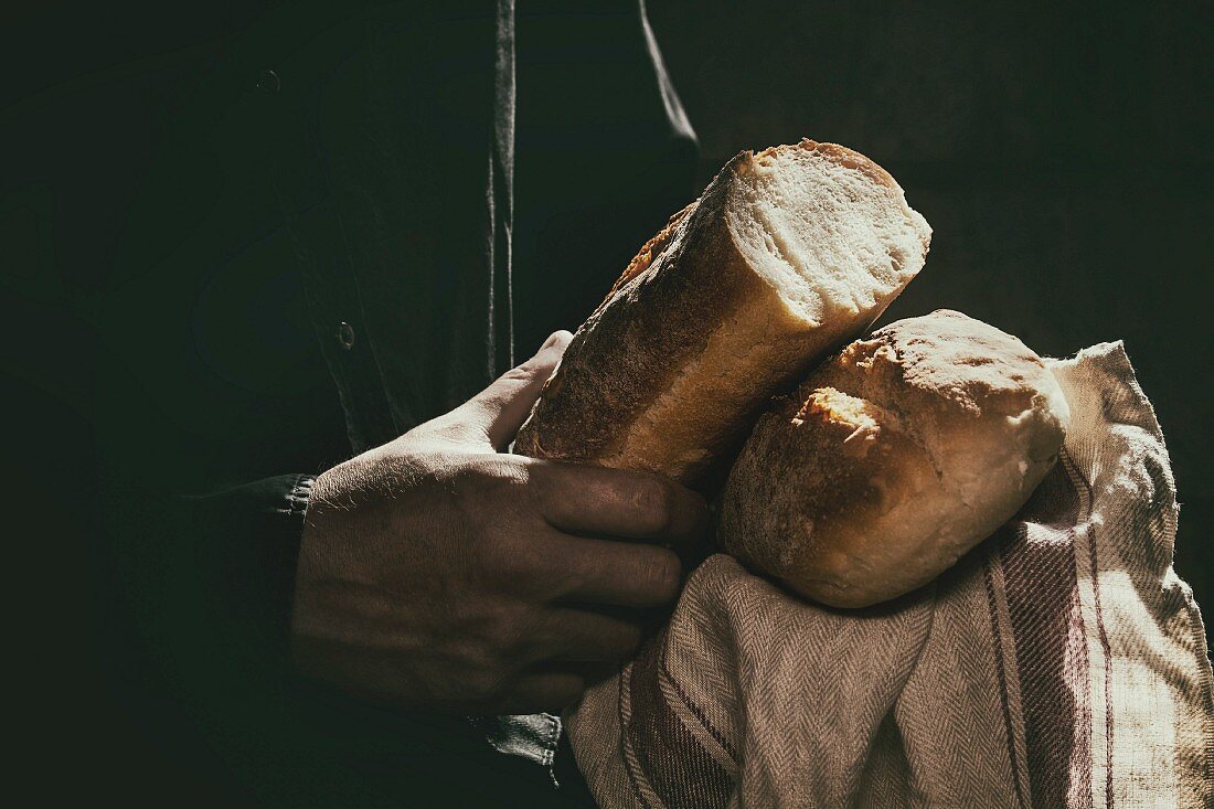 Männerhände halten zwei Laibe frisch gebackenes Weizenbrot
