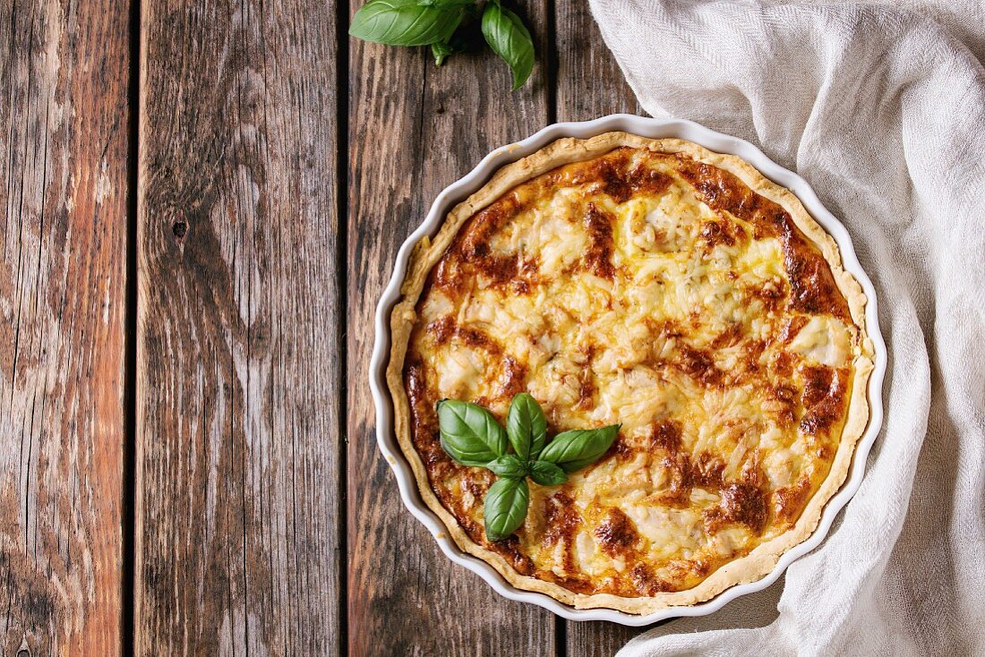 Baked homemade quiche pie in white ceramic form served with fresh greens