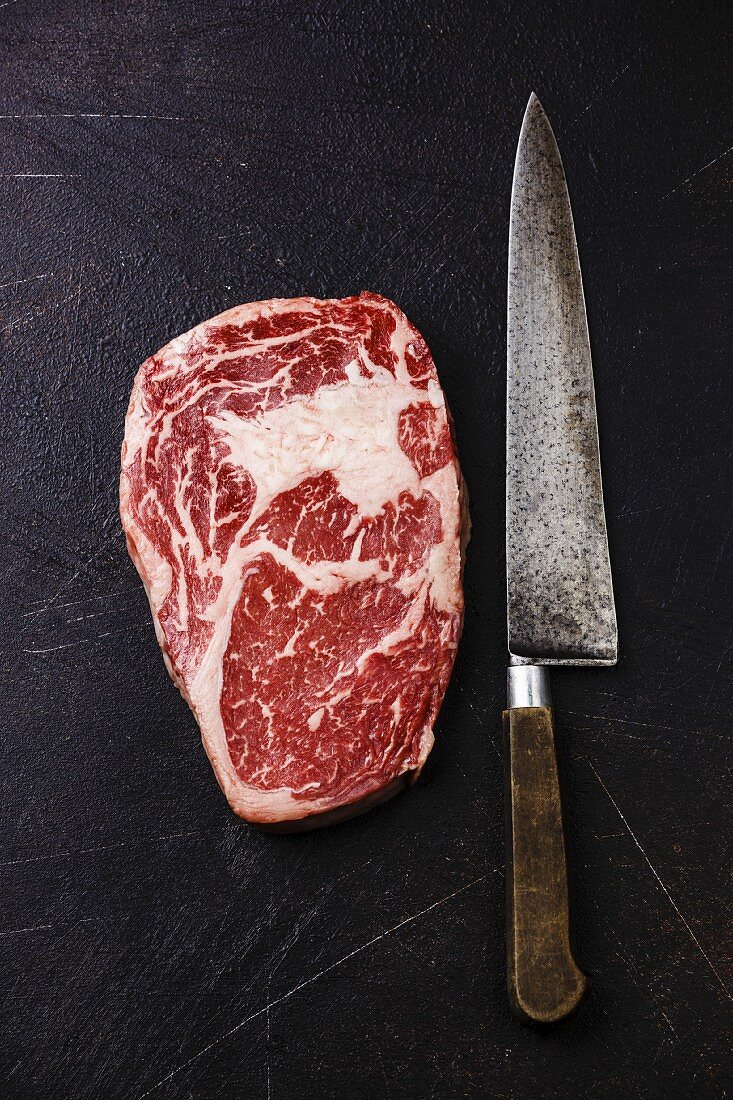 Raw fresh marbled meat Steak Rib eye Black Angus and kitchen knife on dark background