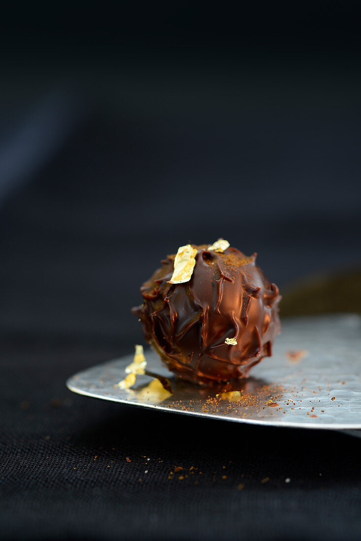 A dark truffle praline decorated with gold leaf