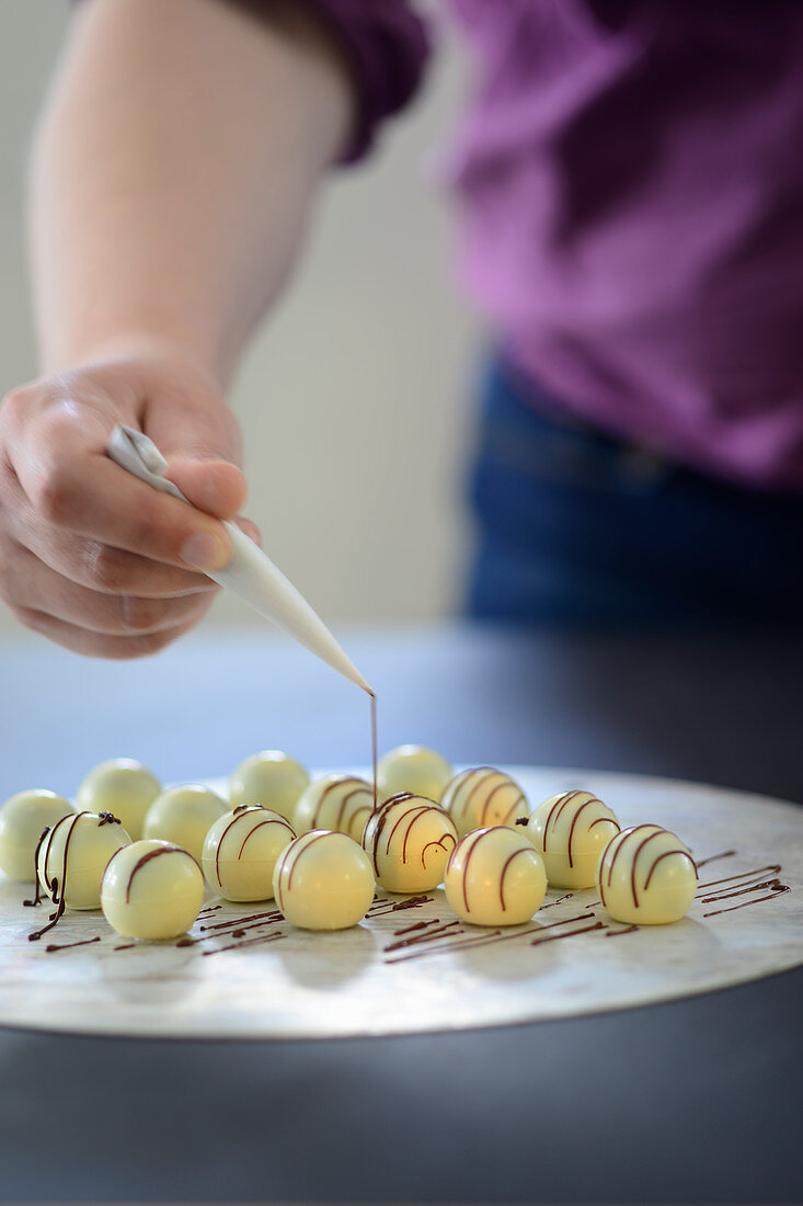 White truffle pralines being decorated with liquid chocolate