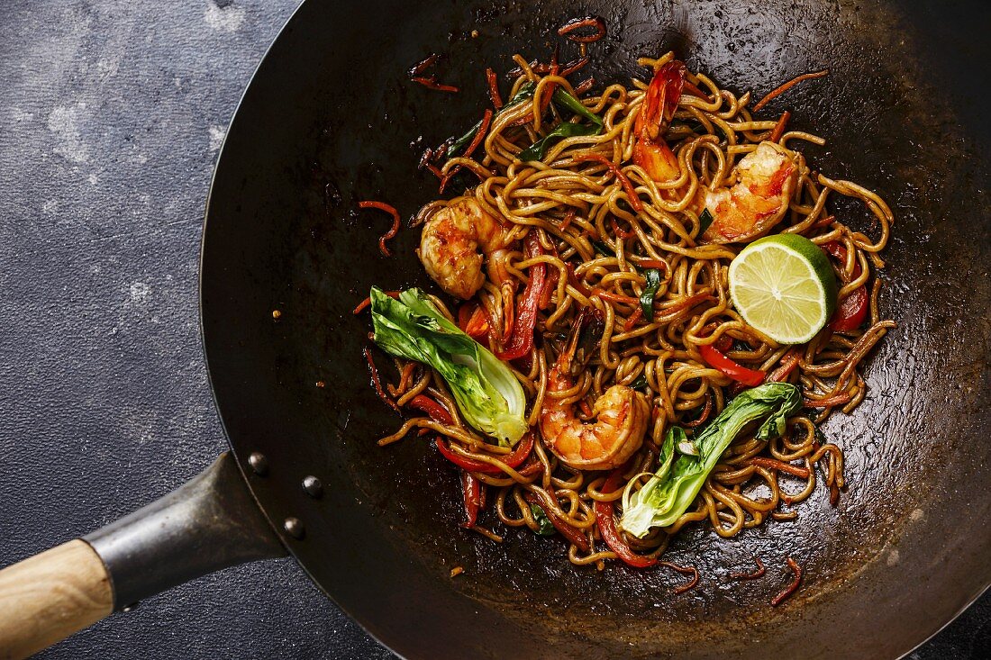 Udon stir-fry noodles with shrimp in wok pan on dark stone background