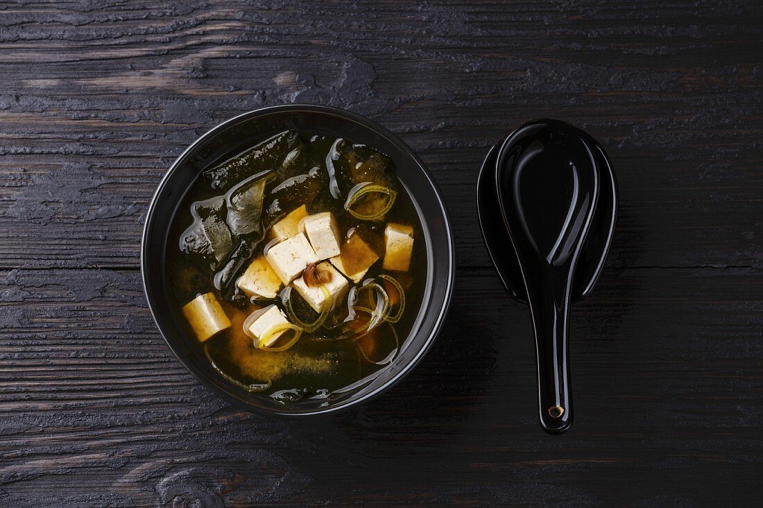 Miso Soup with tofu and wakame in bowl serving size on burned black wooden background
