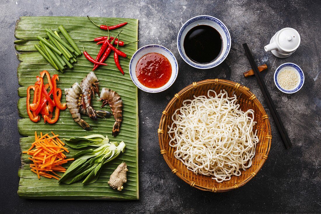 Ingredients for cooking Udon noodles with Tiger shrimps, greens, vegetables, spices on banana leaf on dark background