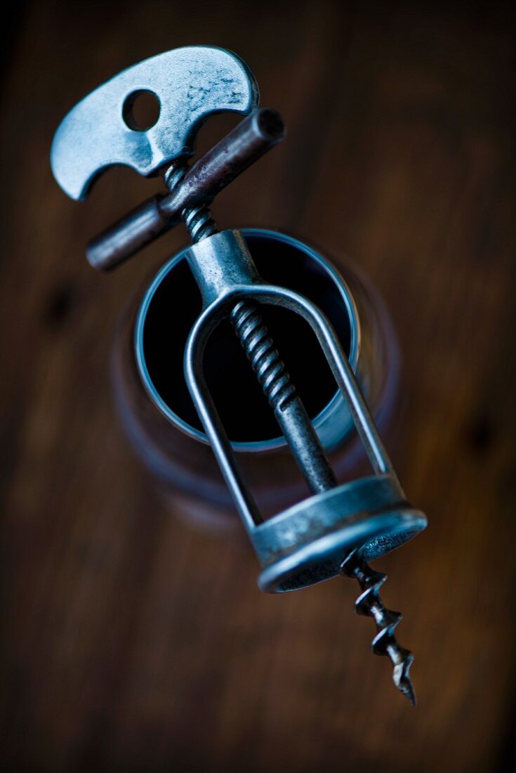 An antique corkscrew on top of a glass of red wine