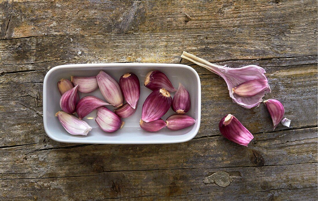 Fresh garlic cloves in a white dish on a wooden surface