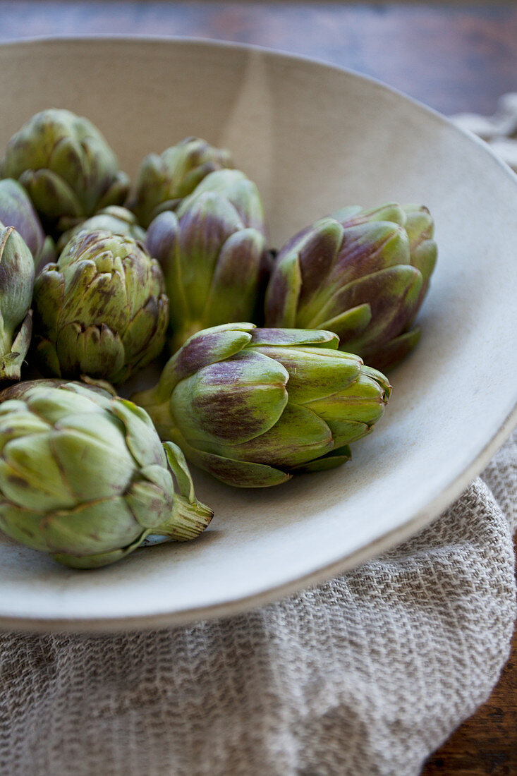 Artichokes in a beige bowl with a beige towel underneath