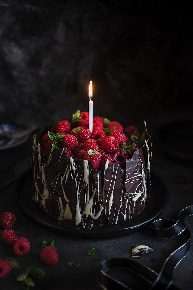 Schokoladenkuchen mit Himbeeren, Schokoladenblättern und Kerze