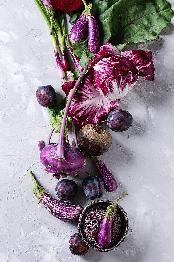 Stillleben mit lilafarbenem Gemüse und Obst auf weißem Untergrund (Aufsicht)