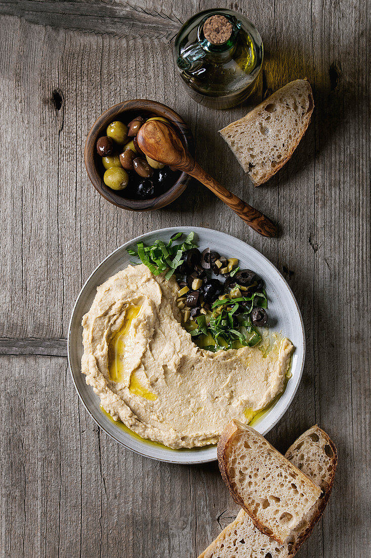 Hummus serviert mit Oliven und Brot (Aufsicht)