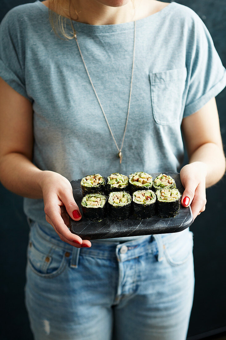 Frau serviert 'No Rice' Veggie-Sushi mit Avocado, Gurke und Räuchertofu