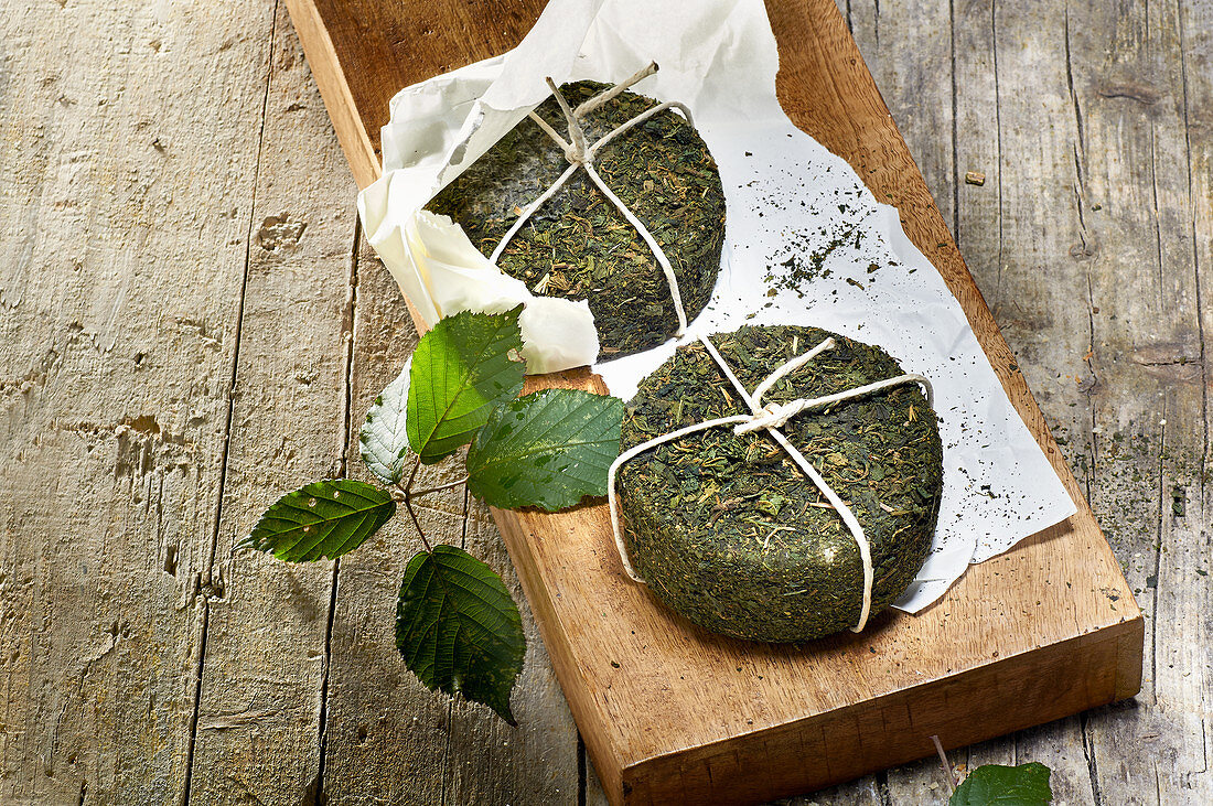 Two pecorino cheeses with stinging nettle rind on a wooden board