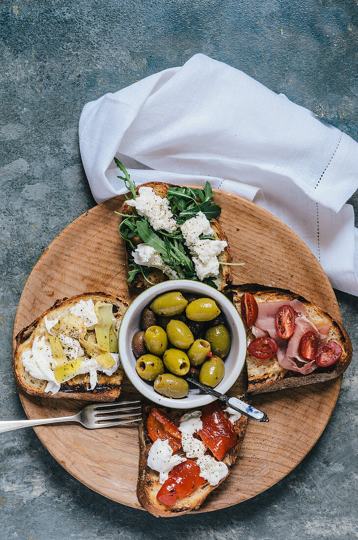 Various bruschettas and olives on a wooden plate